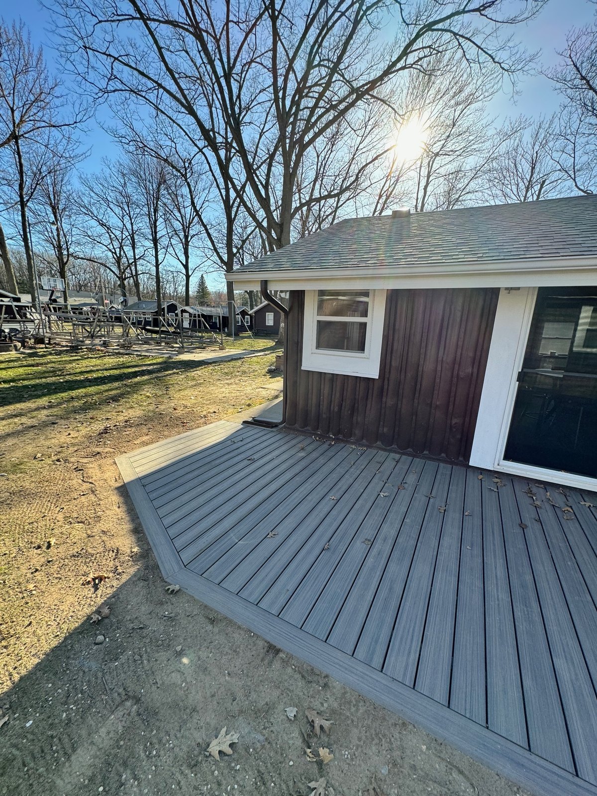 Gray composite deck wrapping a lakeside home with stone chimney